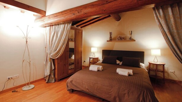 Ein Schlafzimmer mit Holzbalkendecke, einem großen Bett mit Kissen, zwei Nachttischlampen und einem Schrank mit Spiegel.