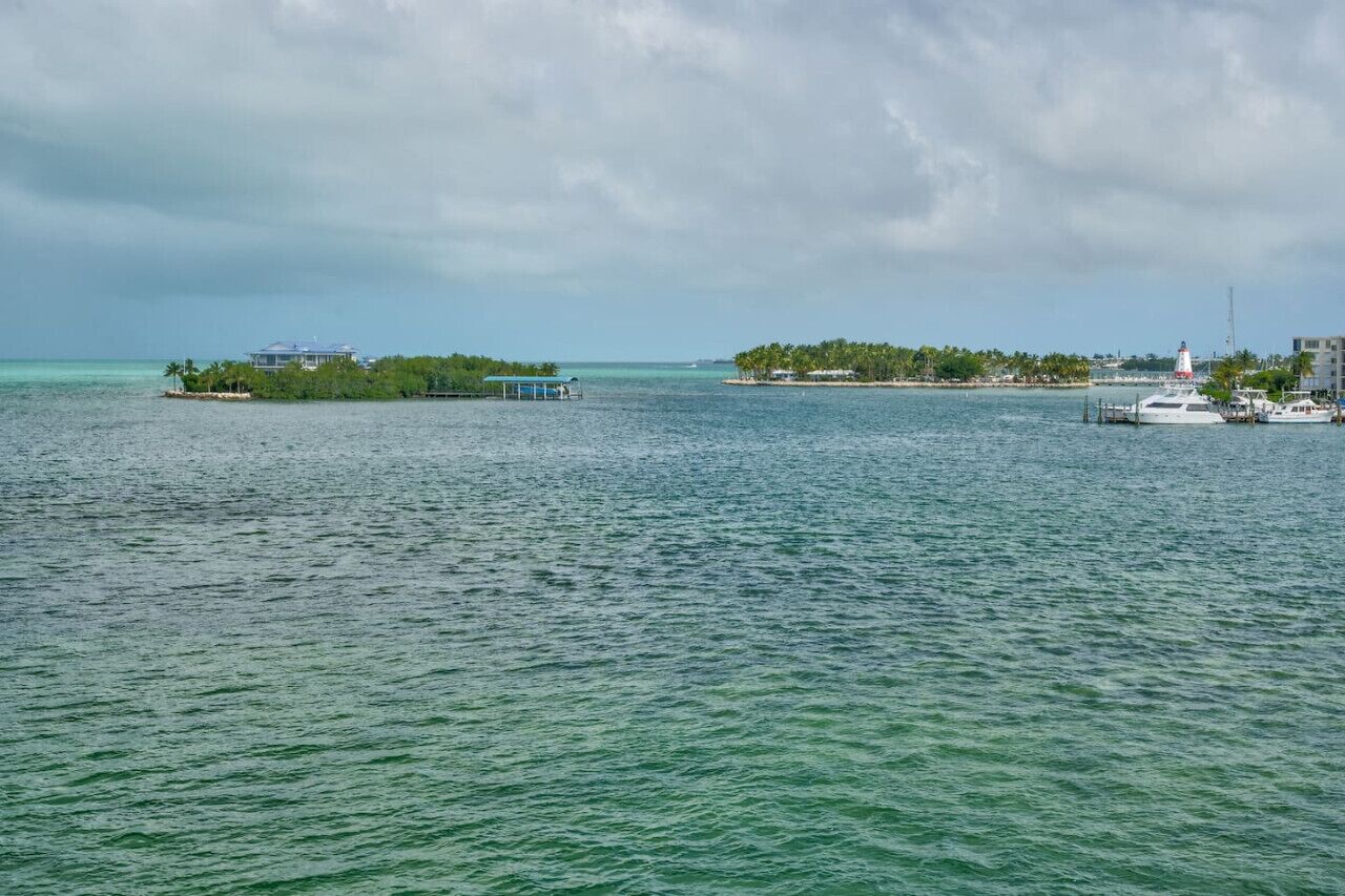 A marina with boats docked, a small island with buildings, and a lighthouse in the distance.