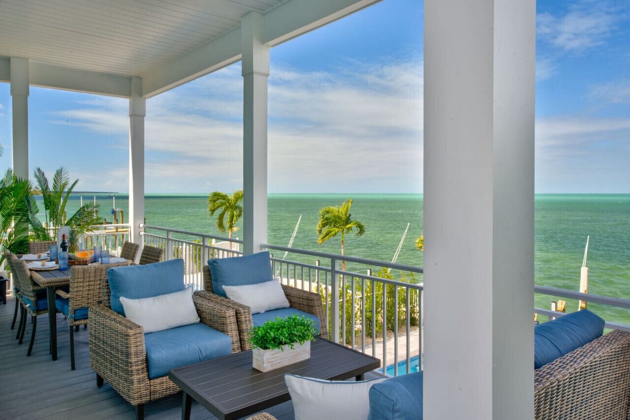 A covered outdoor area with wicker furniture, a table with a plant, and a view of the ocean.