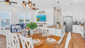 A modern kitchen with white cabinets, a large island, and a dining area with white chairs and a wooden table. - World-Class Oceanfront Pool/Hot tub Sunset Escape `The Lighthouse` (Marathon)