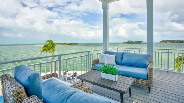 A covered outdoor area with wicker furniture, a table with a plant, and a view of the ocean and islands. - World-Class Oceanfront Pool/Hot tub Sunset Escape `The Lighthouse` (Marathon)