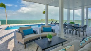 A covered outdoor area with a pool, lounge chairs, and seating arrangements. - World-Class Oceanfront Pool/Hot tub Sunset Escape `The Lighthouse` (Marathon)