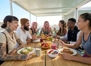 Un grupo de personas sentadas alrededor de una mesa con alimentos para el desayuno, como tostadas, fruta y bebidas.