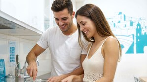 Una pareja preparando comida en una cocina moderna con gabinetes blancos y un mural con vista a la ciudad.