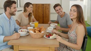 Un grupo de personas sentadas alrededor de una mesa de madera con alimentos para el desayuno, como croissants, fresas y café.