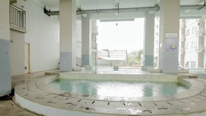 Una piscina circular con borde de azulejos, rodeada de suelo también de azulejos, y una vista de un edificio al fondo.