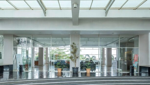 Una entrada de edificio moderna con puertas de vidrio, plantas en macetas y una vista despejada del interior.
