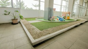 Un espacio interior amplio con un área de juegos de césped artificial verde, una casita y una planta en maceta.
