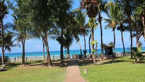 Un sendero pavimentado que conduce a una playa con palmeras y una valla de madera.