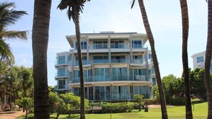 Un hotel de varios pisos con un diseño arquitectónico moderno, rodeado de palmeras y un césped cuidado.