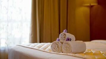 A neatly made bed with rolled towels and a small decorative item on it.