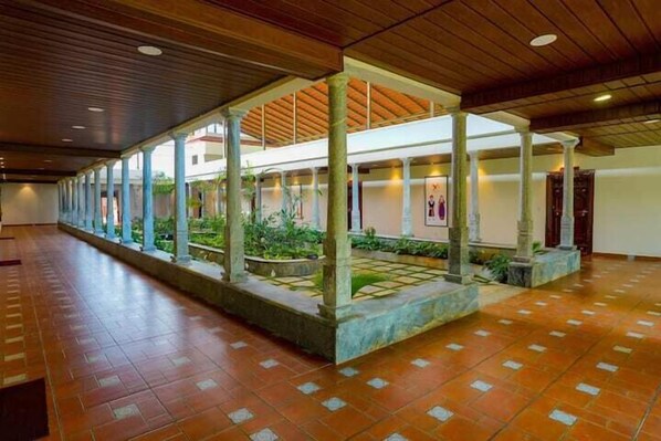 A spacious corridor with a tiled floor and a covered area with columns and plants. - The Windchimes Retreat (Virajpet)