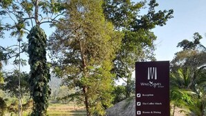 En skylt som listar olika bekvämligheter, inklusive reception, kafé, rum och matsal, lekplats för barn och plats för lägereld, parkeringsplats, avlämningsplats, en bäck och en naturstig.