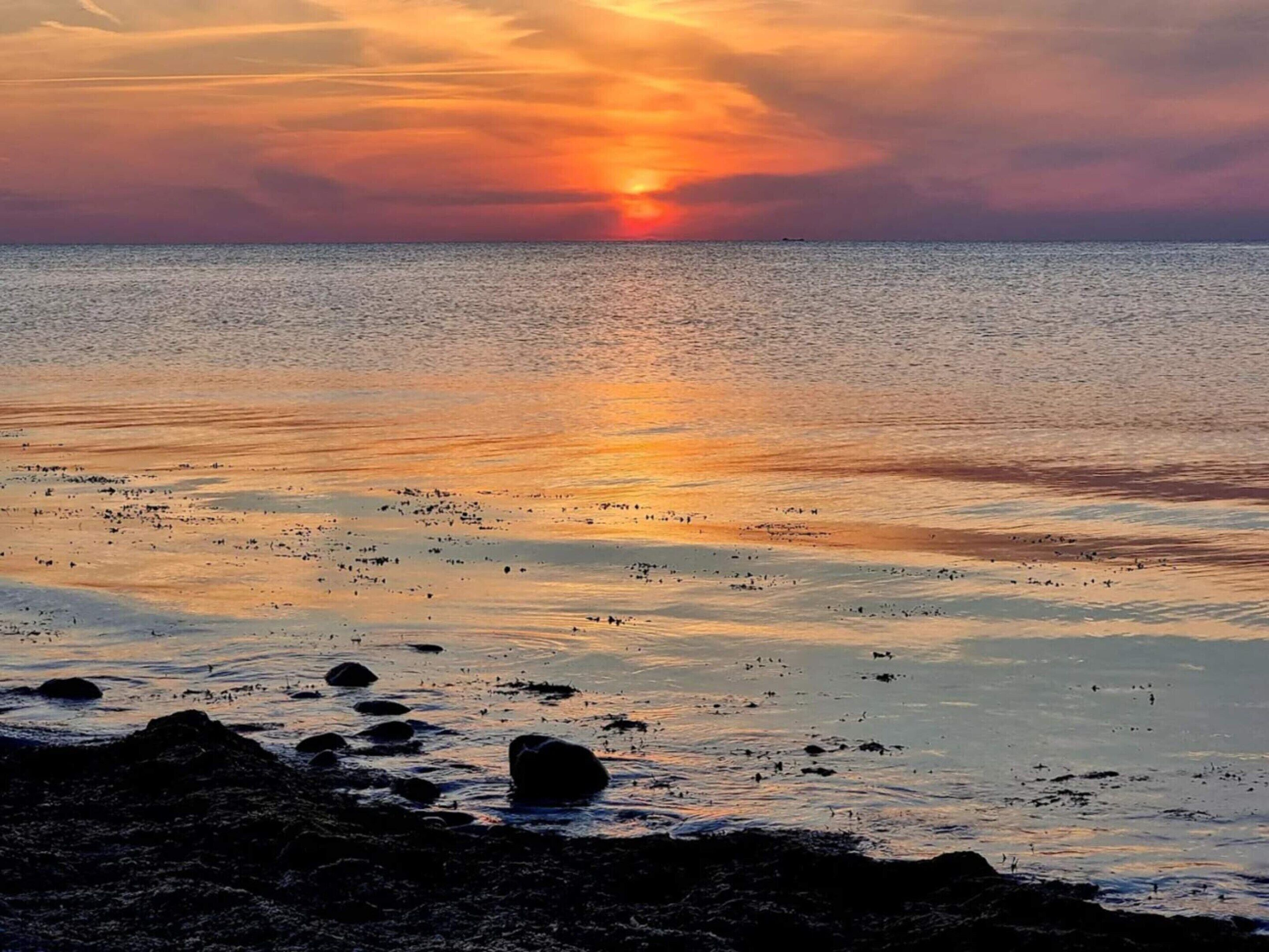 A sunset over a calm sea with rocks in the foreground.