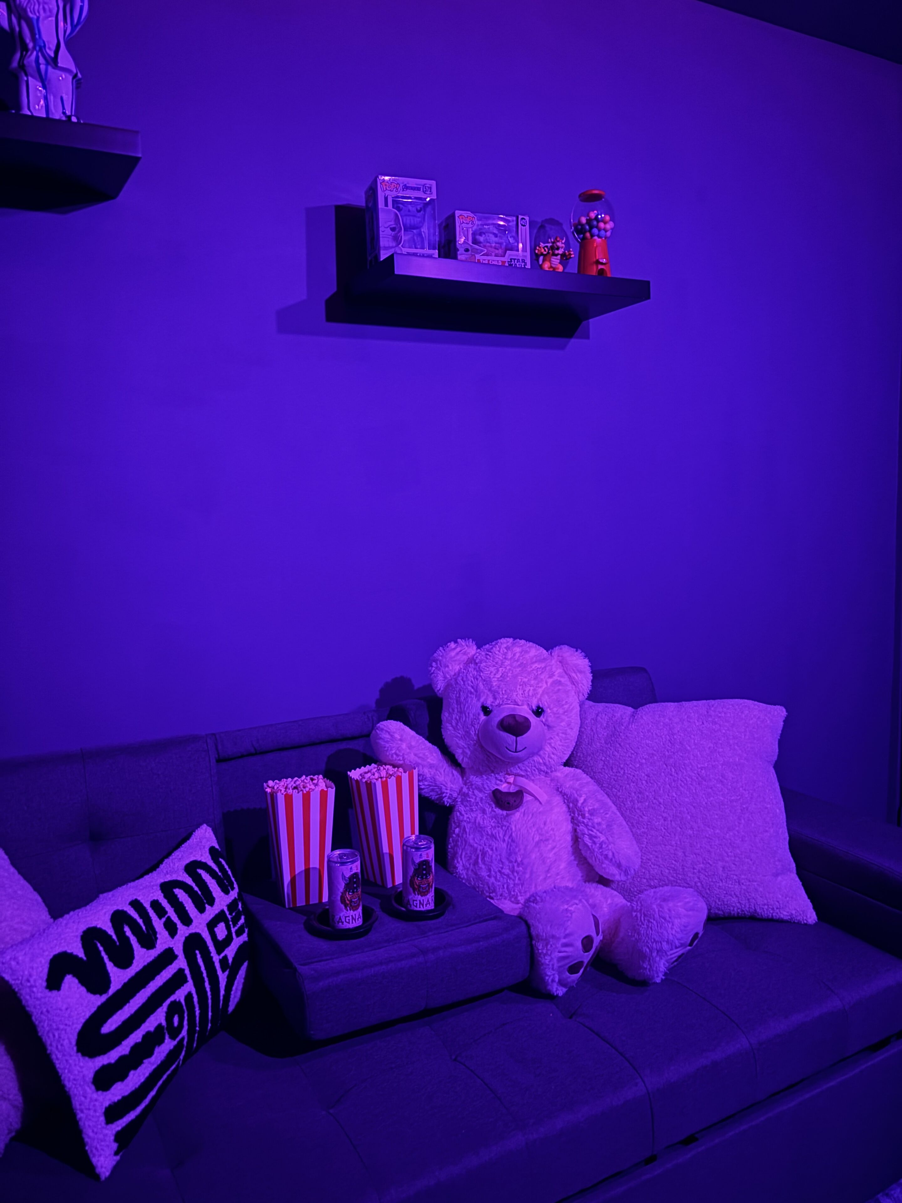 A room with a sofa, a teddy bear, popcorn, and a shelf with collectibles.