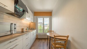 Uma cozinha compacta com forno embutido, mesa de jantar com cadeiras e janela com vista para edifícios.