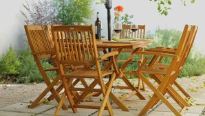 Un conjunto de comedor exterior de madera con sillas y una mesa, una botella de vino y un jarrón con flores.