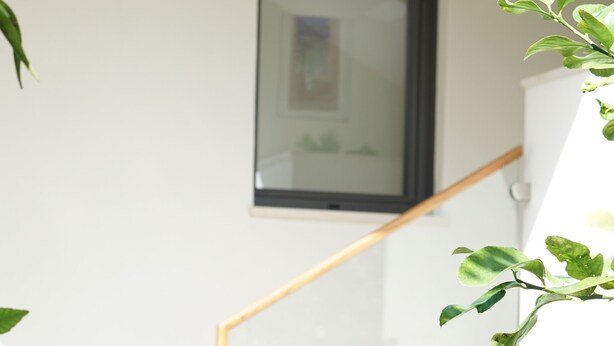 Un escalier avec des rampes en verre et des marches en bois, menant à l’étage supérieur.