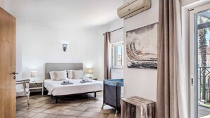 A bedroom with a bed, bedside tables, a window, and a view of the outside.