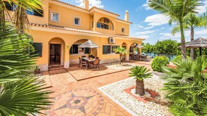 A yellow building with a tiled patio, outdoor seating, and palm trees.