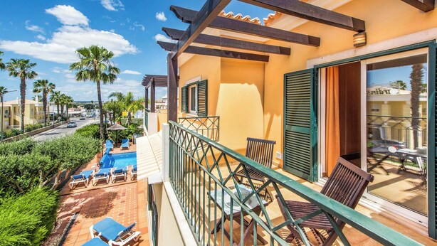 A balcony with a pool, outdoor furniture, and a view of palm trees and buildings.