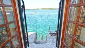 Una escalera de piedra conduce a una terraza de madera con vistas a un cuerpo de agua y un barco a lo lejos.