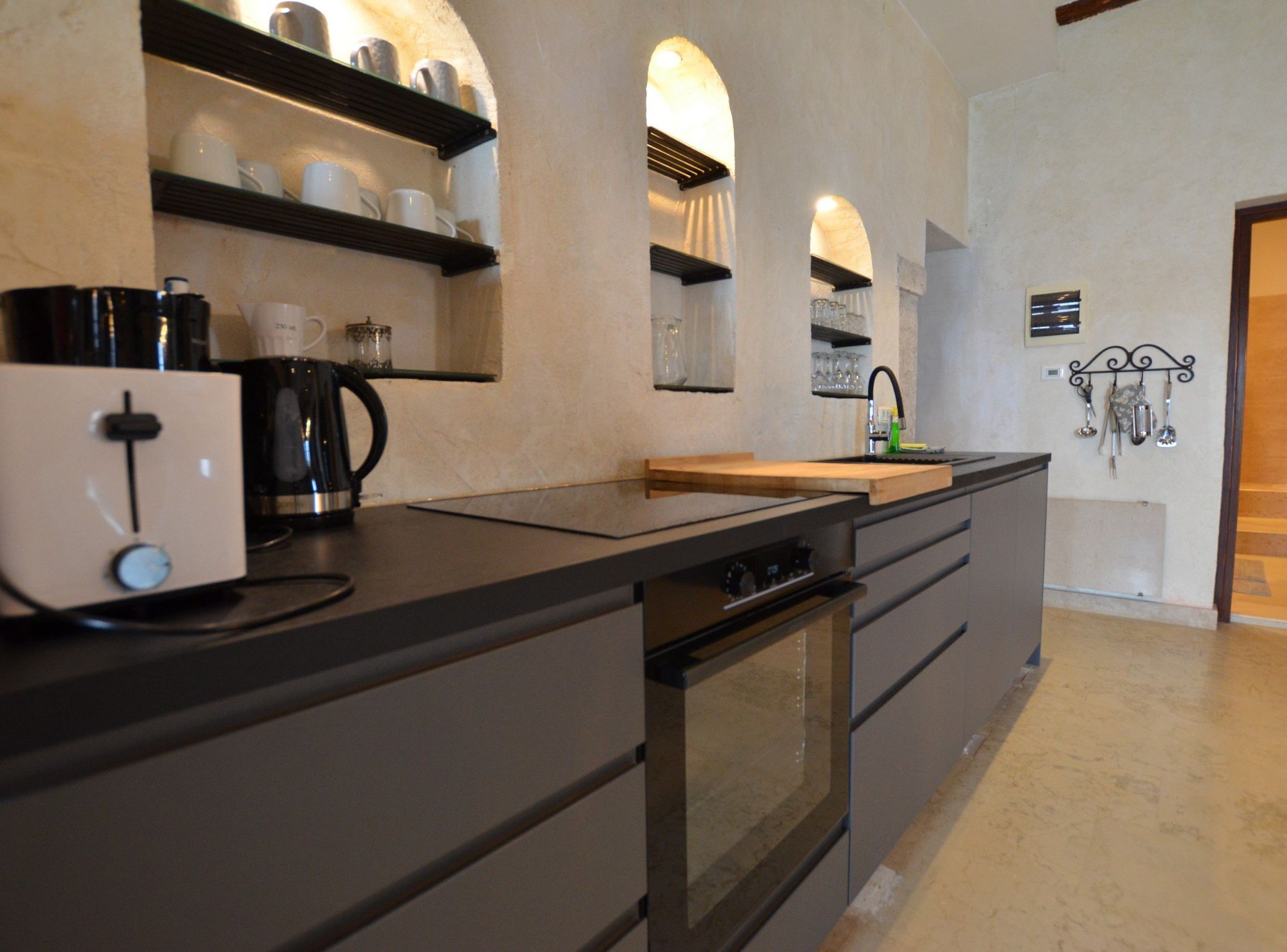 A modern kitchen with a black countertop, built-in oven, and shelves with cups and glasses.
