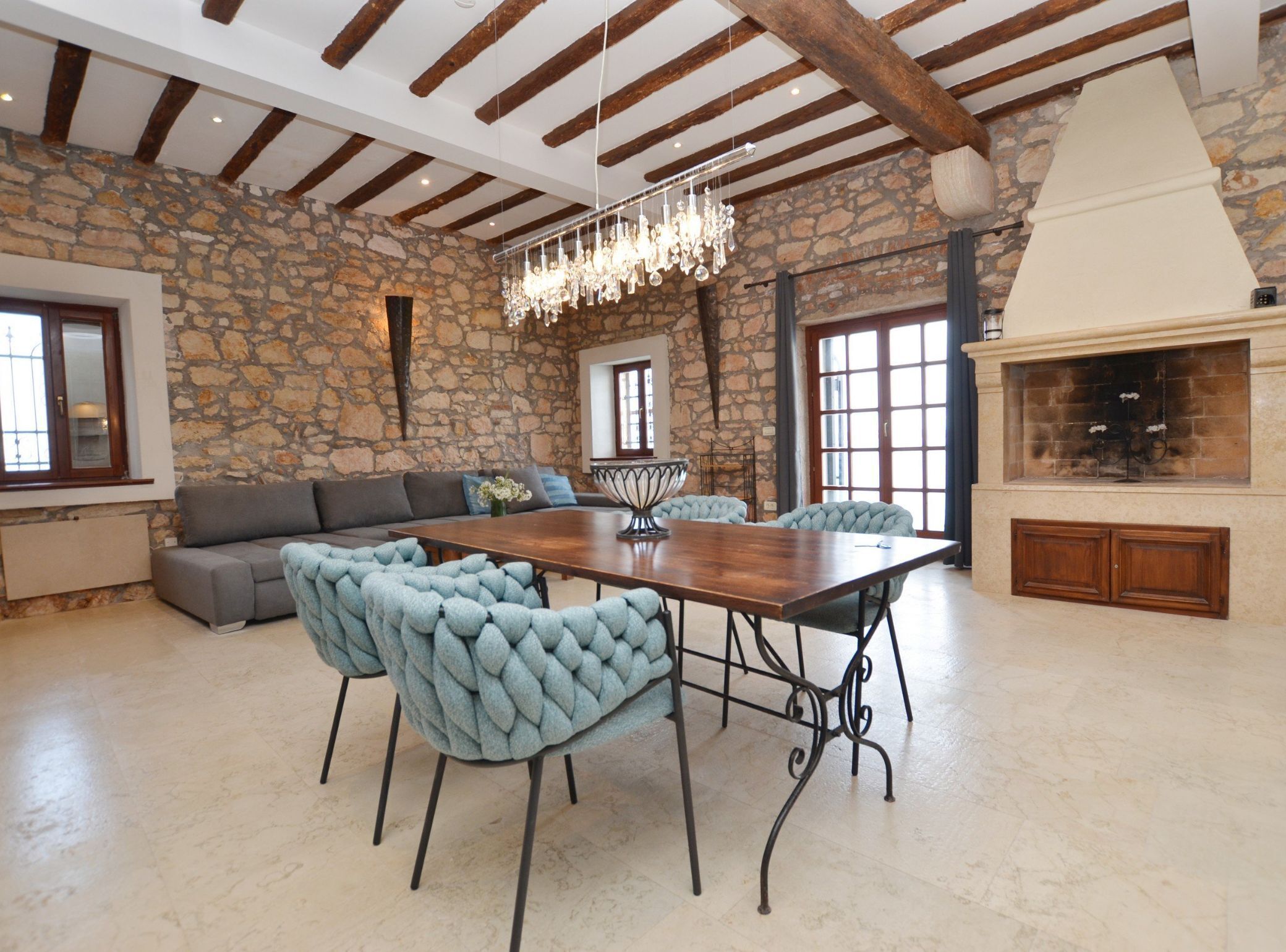 Une pièce spacieuse avec un mur en pierre, un plafond en bois, une grande table à manger entourée de chaises et une cheminée.