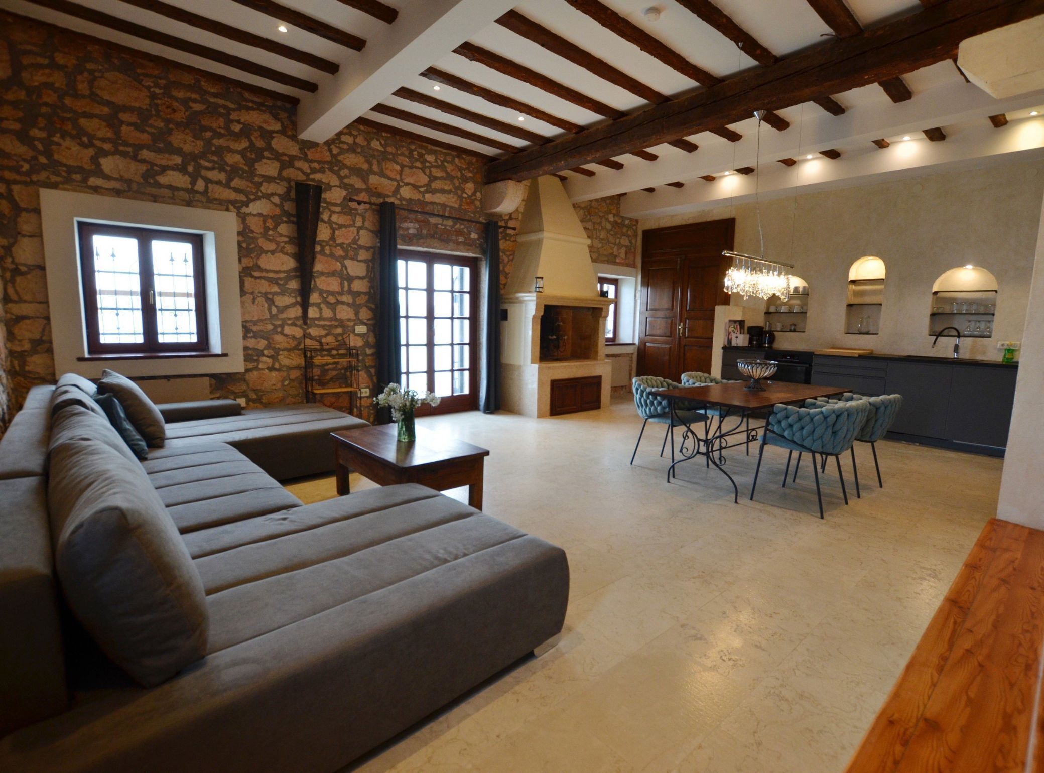 A spacious living area with a stone wall, a large sofa, a dining table with chairs, and a kitchen area with a bar.
