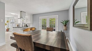 A modern kitchen with white cabinets, a large island, and a dining area with a wooden table and chairs. - Sunset Heights Retreat- 3 Stylish & Spacious Bedroom (Fort Worth)