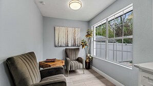 A room with a gray sofa, a chair, a wooden table, and a large window with a view of trees. - Sunset Heights Retreat- 3 Stylish & Spacious Bedroom (Fort Worth)