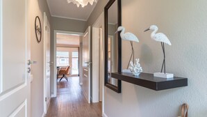 A hallway with a wooden floor, a black floating shelf with decorative items, and a mirror reflecting a white bird sculpture. - Apartment in Busum Near Perlebucht Lagoon (Westerdeichstrich)