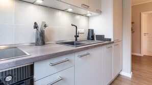 A modern kitchen with white cabinets, a stainless steel sink, and a built-in stove. - Apartment in Busum Near Perlebucht Lagoon (Westerdeichstrich)
