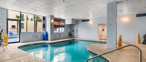 A swimming pool with a lifeguard chair, a no diving sign, and a wet floor sign.
