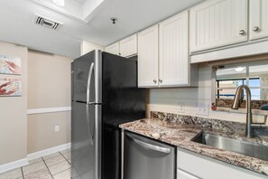 A kitchen with a stainless steel refrigerator, white cabinets, a granite countertop, and a stainless steel sink.