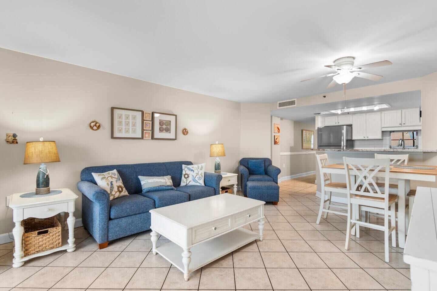 Ein Wohnzimmer mit einem blauen Sofa, einem weißen Couchtisch und einem Essbereich mit weißen Stühlen und einem Holztisch.