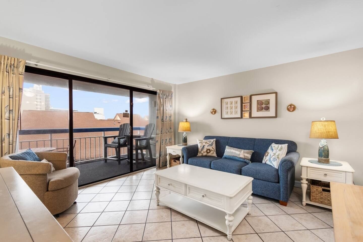 Un salon avec un canapé, une table basse, un balcon avec des chaises et une vue sur les immebles.