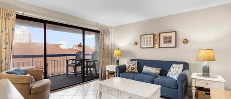 Un salon avec un canapé, une table basse, un balcon avec des chaises et une vue sur les immebles.