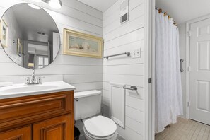 A bathroom with a white vanity, a toilet, a shower with a white curtain, and a framed picture on the wall. - Luxury Ocean View Condo- Relaxing Exclusive Access (Myrtle Beach)