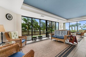 A spacious indoor area with wicker furniture, large windows, and a view of the outdoors. - Luxury Ocean View Condo- Relaxing Exclusive Access (Myrtle Beach)