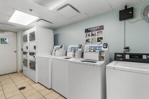A laundry facility with multiple washing machines and dryers, a control panel, and a wall-mounted fan.
