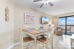 A dining area with a wooden table and chairs, a ceiling fan, and a view of the sea through large windows. - Luxury Ocean View Condo- Relaxing Exclusive Access (Myrtle Beach)