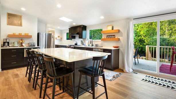 A modern kitchen with a central island, black bar stools, and a sliding glass door leading to a deck.