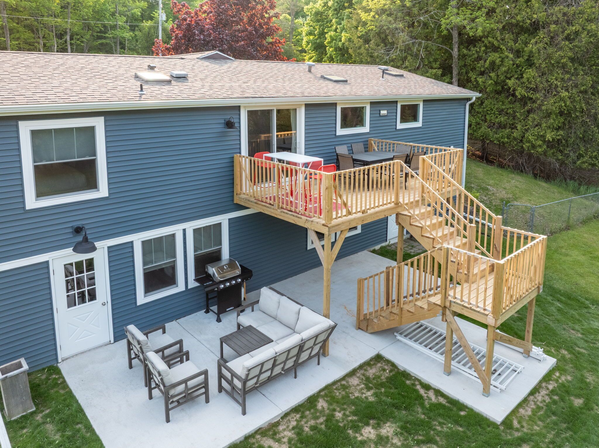 A two-story house with a deck, outdoor seating, and a grill area.