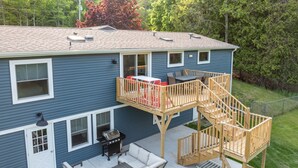 A two-story house with a deck, outdoor seating, and a grill area.