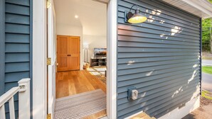 A house with a wooden door, a light fixture on the exterior wall, and a visible interior with a wooden floor and a door.