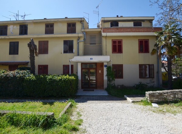A two-story building with a central entrance, a small garden area, and a gravel driveway. - Airy and Comfortable Apartment With Loggia (Rovinj)