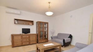 Ein Wohnzimmer mit einem Holzkasten, einem Fernseher, einem grauen Sofa und einem Couchtisch aus Holz.