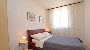 Ein Schlafzimmer mit einem Bett, zwei Nachttischlampen, einem kleinen Tisch und einem Fenster mit Vorhängen.