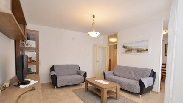 Ein Wohnzimmer mit zwei grauen Sofas, einem Holztisch, einem Fernseher auf einem Holzständer und einem Gemälde an der Wand.